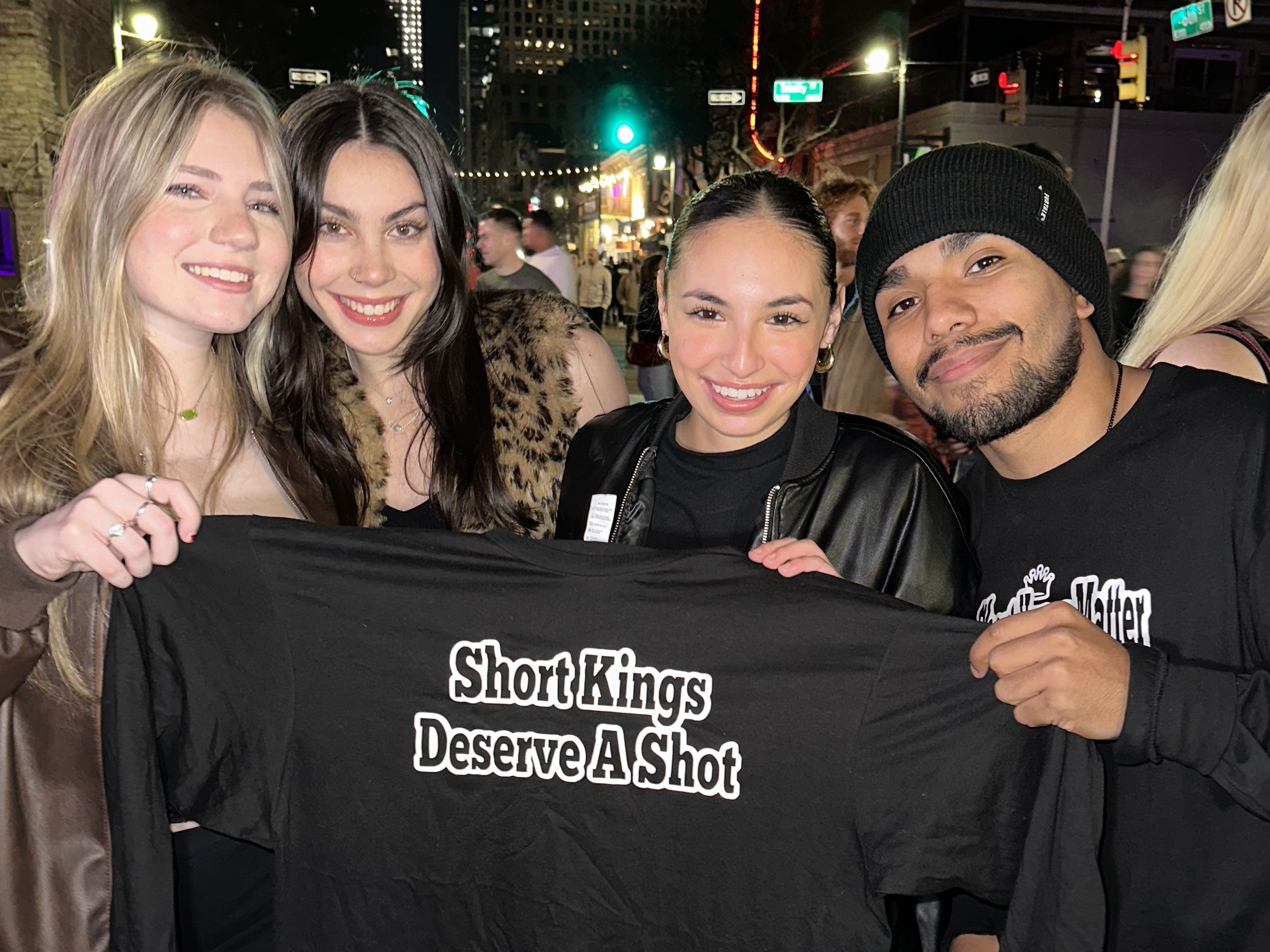 Israel Padilla chilling with 3 baddies, holding up the new Short Kings Deserve a Shot sweatshirt